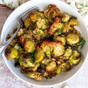 White bowl with brussel sprouts covered in Parmesan, silver fork in the bowl.