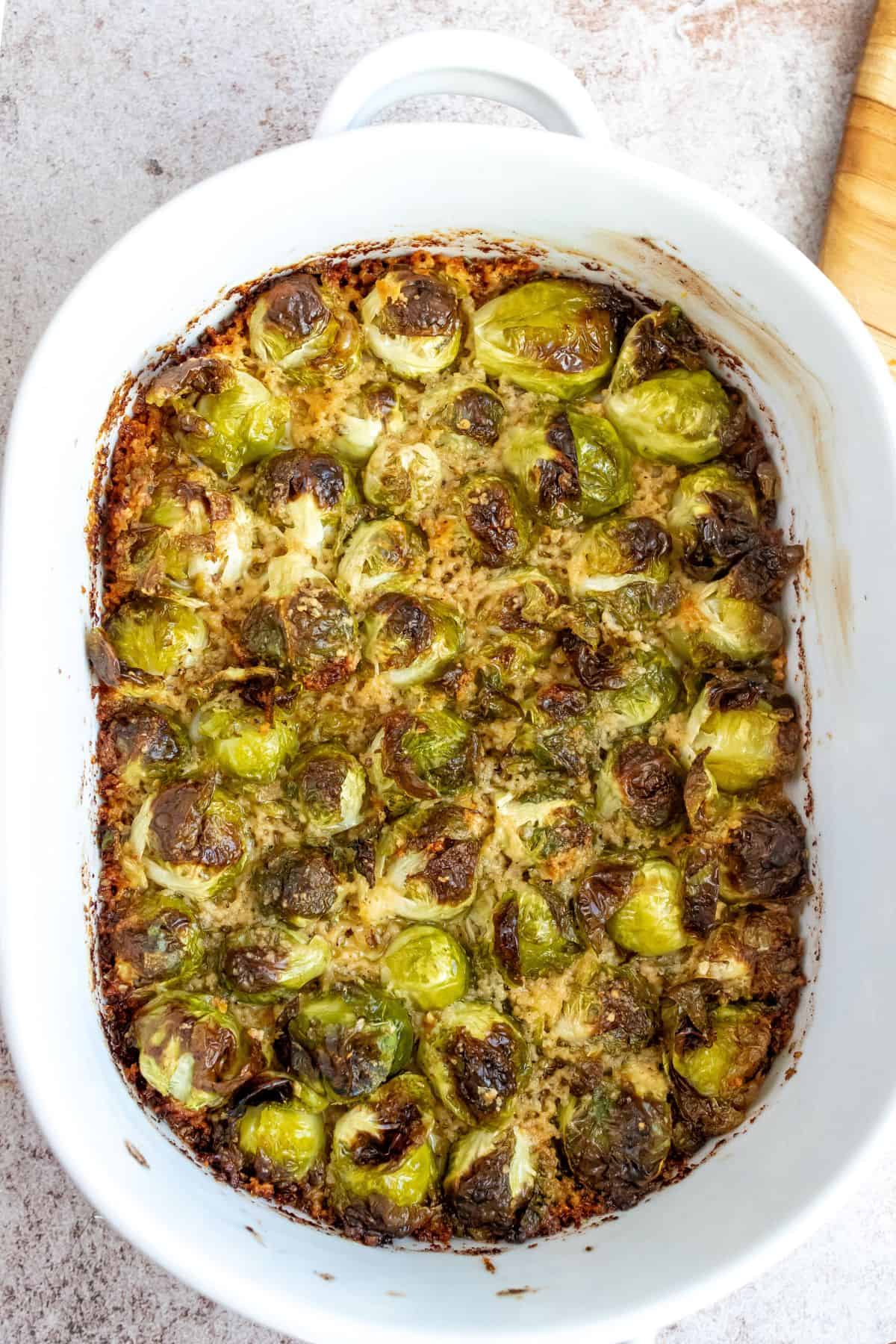 White baking dish with brussel sprouts and Parmesan all over them. 