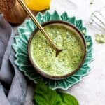 Small bowl with pesto and a gold spoon on a green plate. Fresh basil to the side.