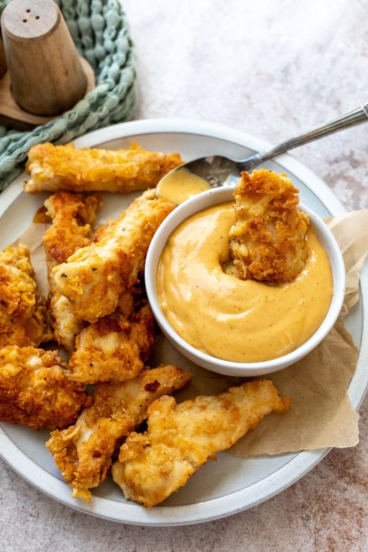 Chicken tenders with spicy honey mustard in a white bowl with a silver soon on the side. 