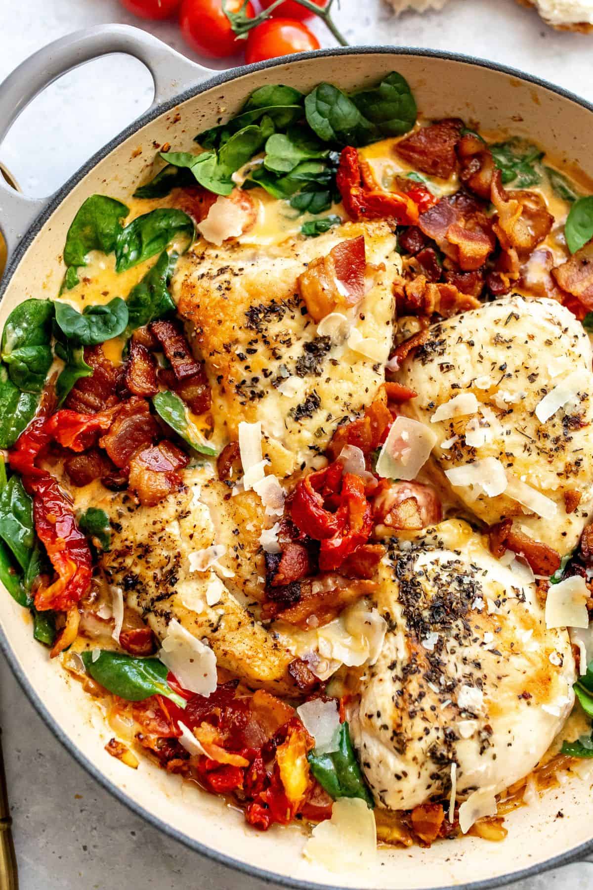 White skillet with Tuscan Chicken in it and a gold spoon to the side up close with seasonings on top. 