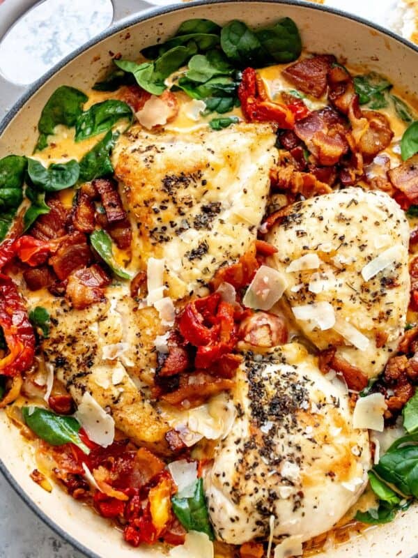 White skillet with Tuscan Chicken in it and a gold spoon to the side.