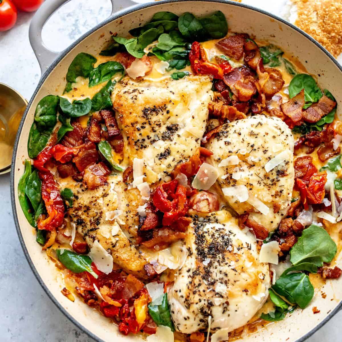 White skillet with Tuscan Chicken in it and a gold spoon to the side.