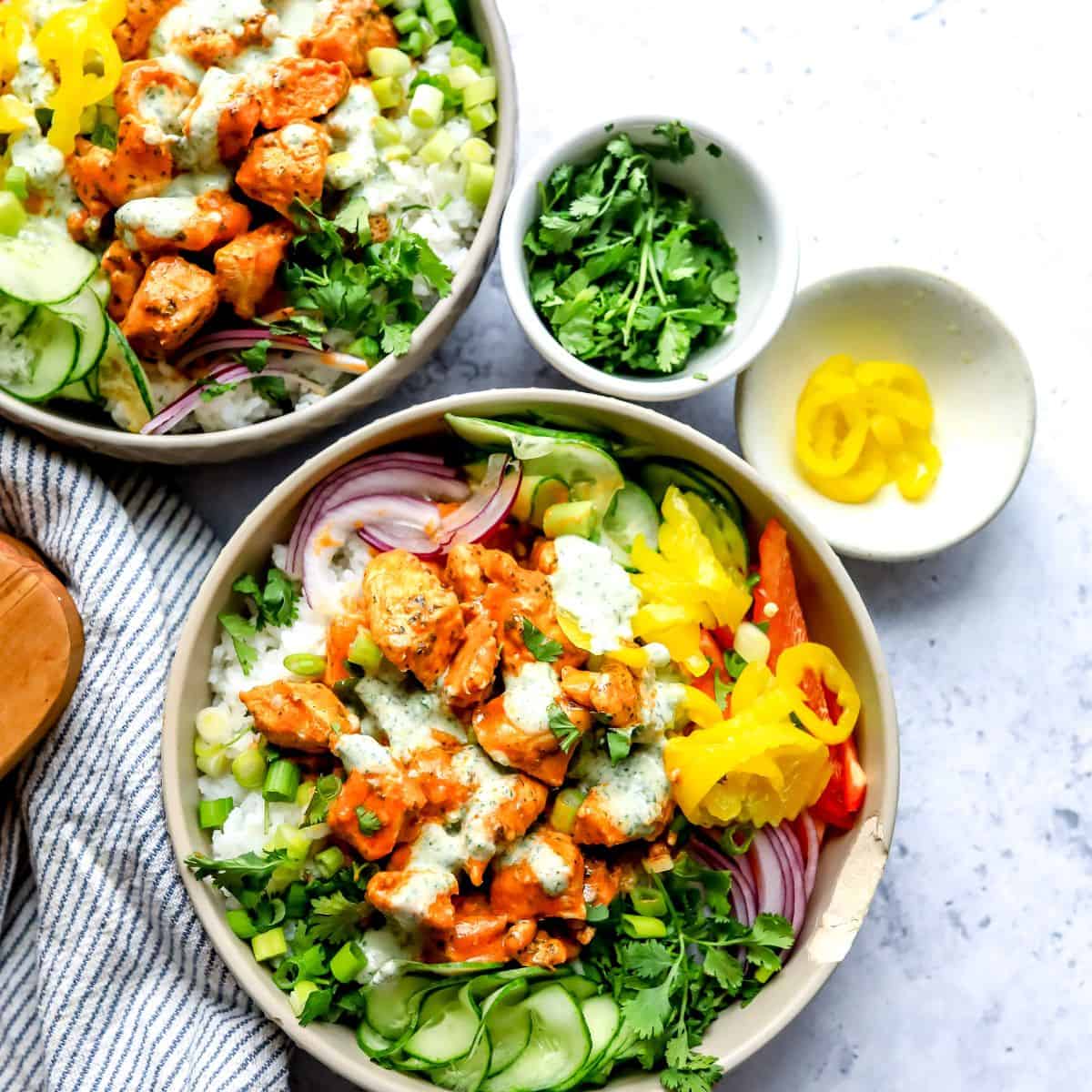 A grey bowl with buffalo sauce. Cucumber to the side with a ranch drizzle.