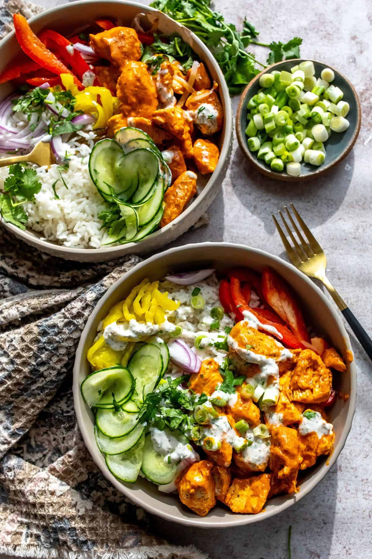 Two grey bowls with and buffalo sauce. Cucumber to the side with a ranch drizzle.