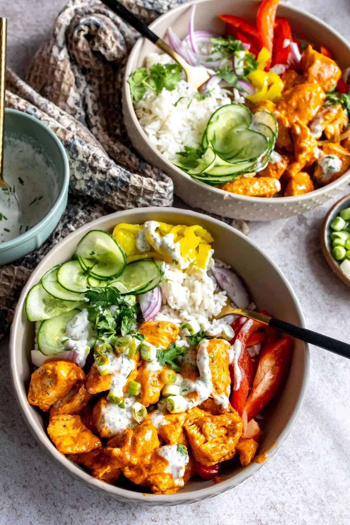 Two grey bowls with and buffalo sauce. Cucumber to the side with a ranch drizzle.