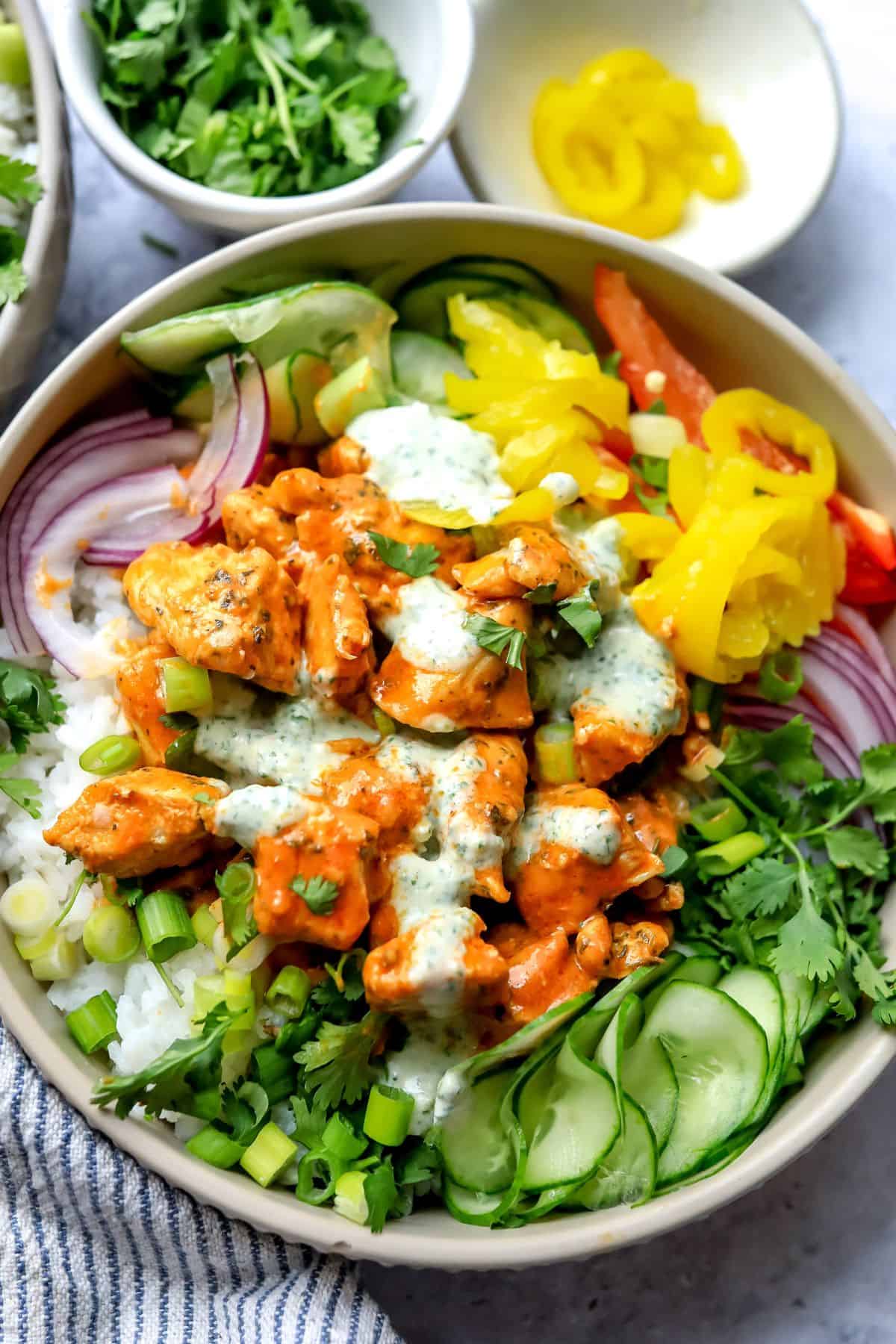 A grey bowl with buffalo sauce. Cucumber to the side with a ranch drizzle.