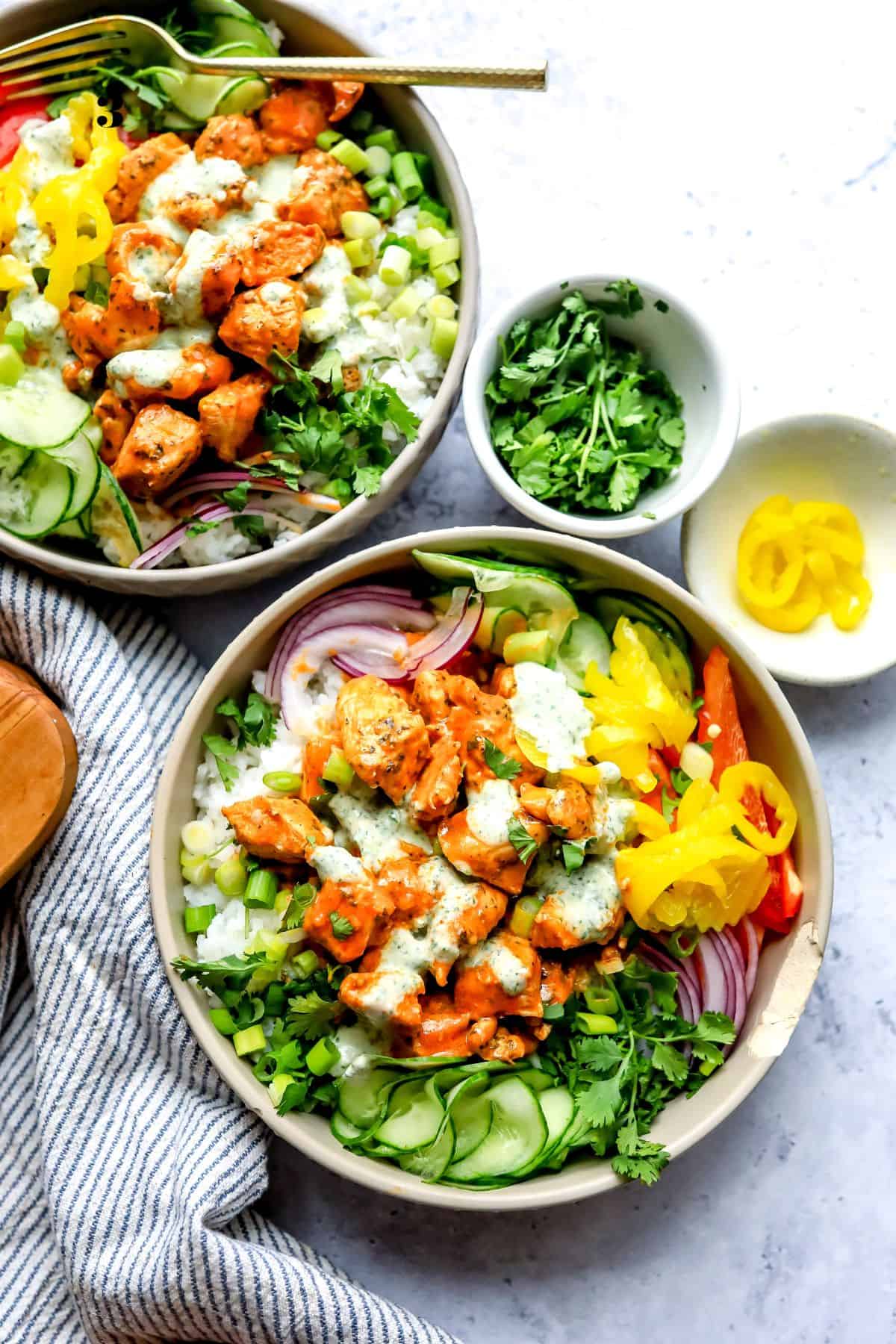 Two grey bowls with and buffalo sauce. Cucumber to the side with a ranch drizzle.
