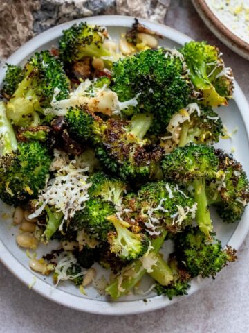 White bowl with charred broccoli and toppings mixed in.