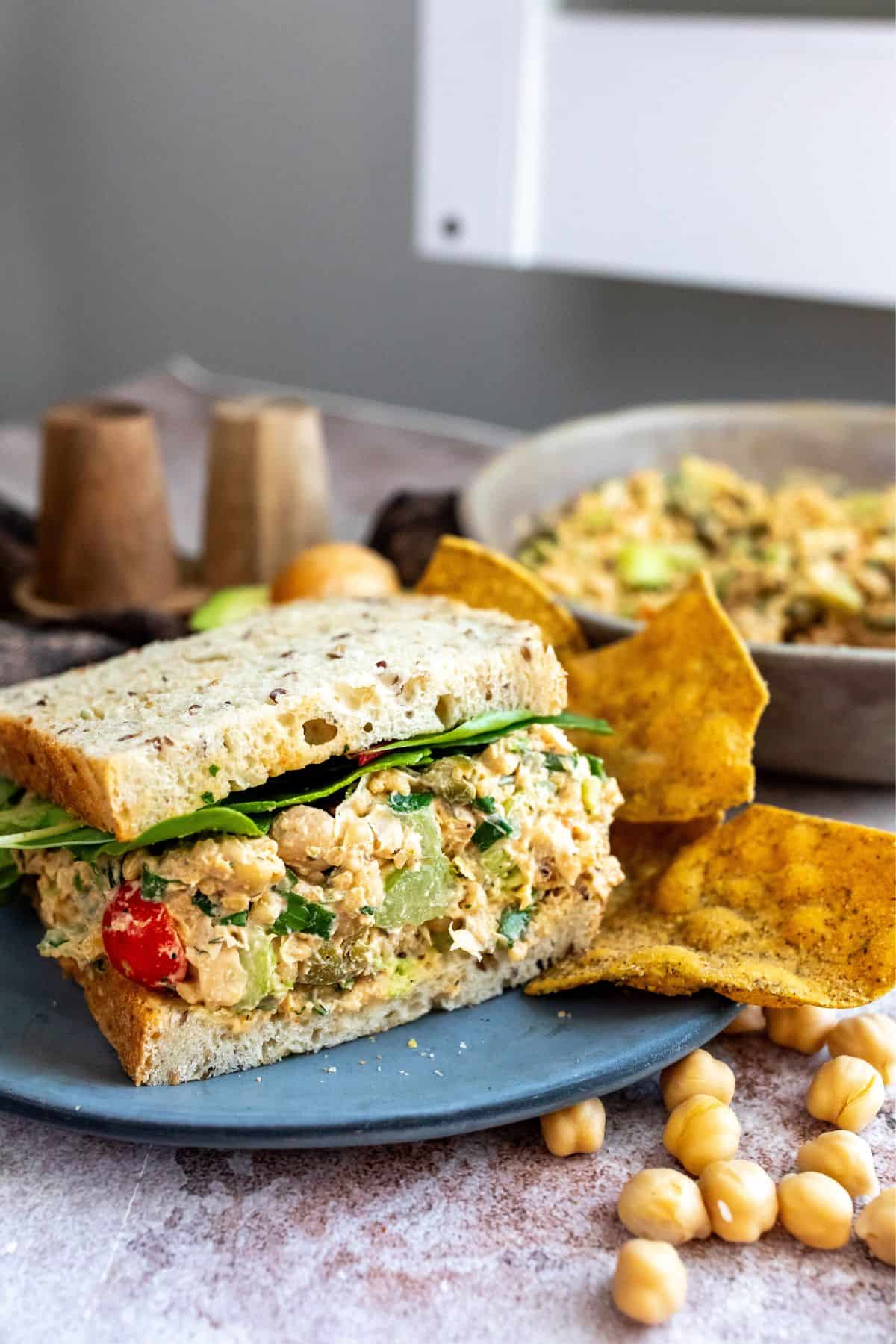 Bread with chickpea salad in the middle. Chips on the side on a grey plate. 