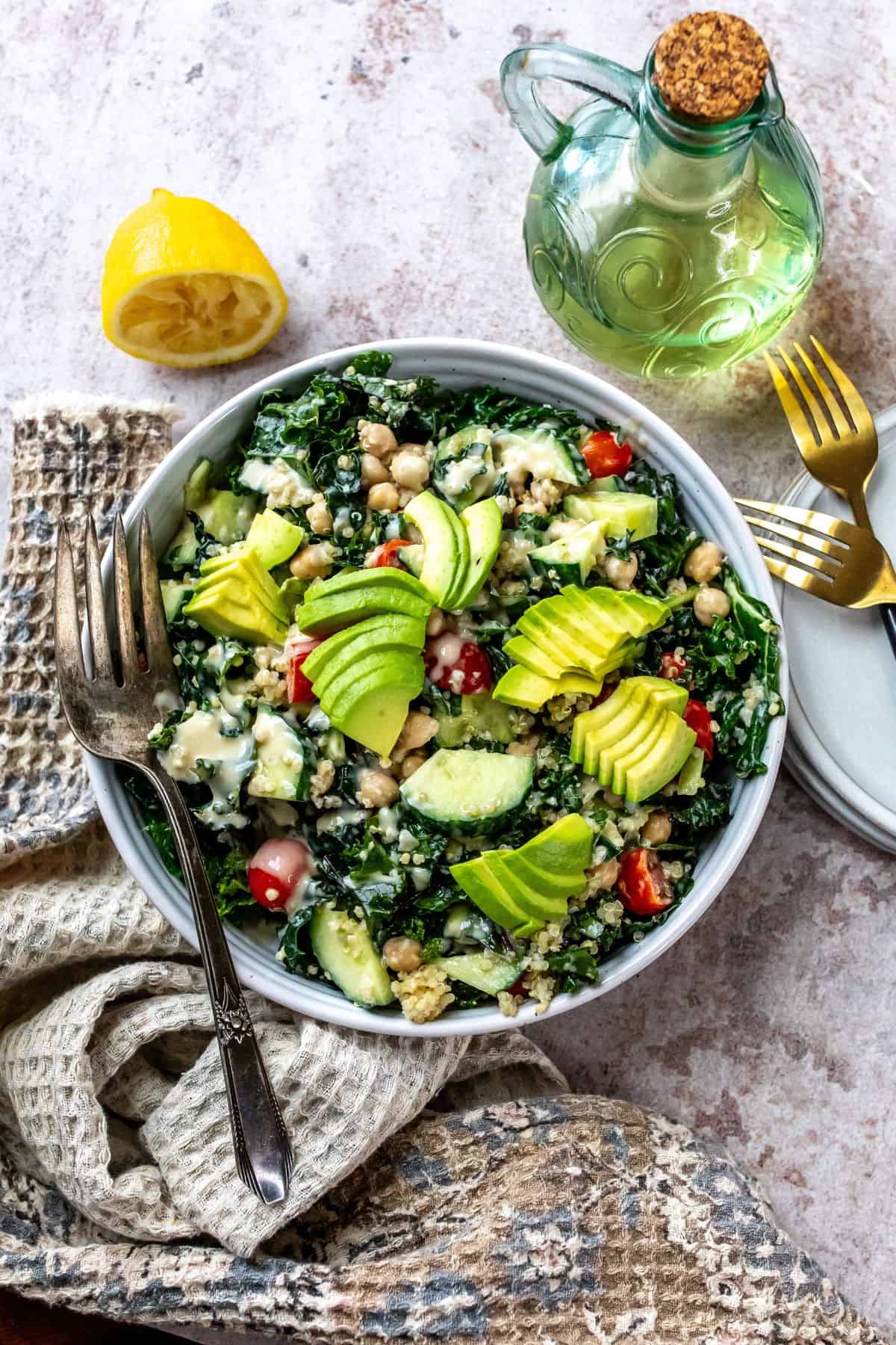 White bowl with kale and chickpeas, loads of veggies and dressing on the top. 