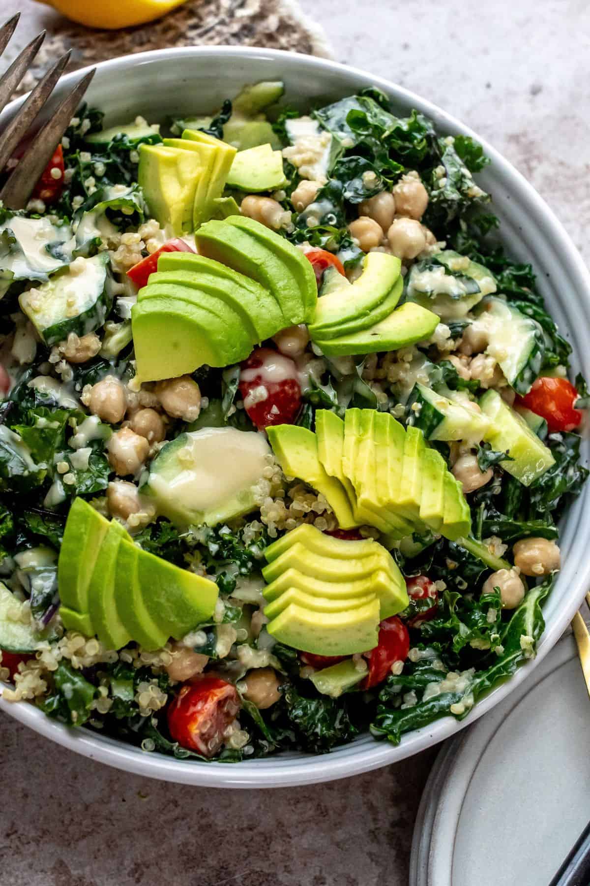 White bowl with kale and chickpeas, loads of veggies and dressing on the top. 
