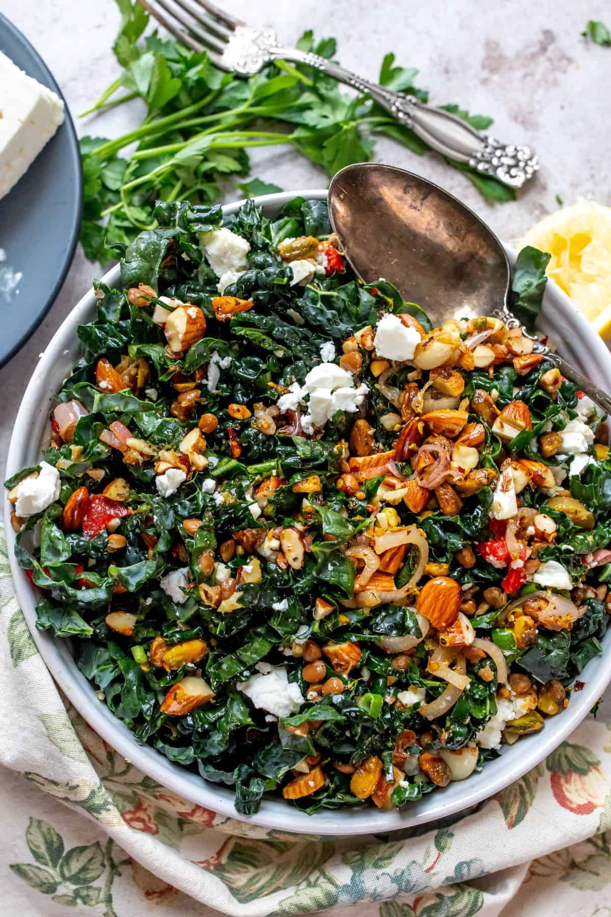 Chopped kale on a speckled plate with a silver spoon on the side. Large silver serving spoon over the salad.