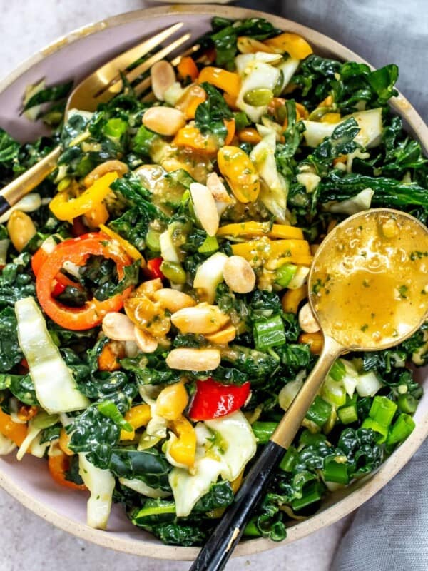 Grey plate with kale and peanuts. Dressing and fork on the side.
