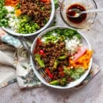 White Ceramic bowls with ground beef and teriyaki sauce. Fresh chopped veggies and a silver fork on the side.