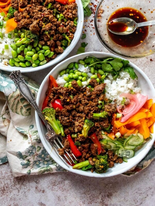 White Ceramic bowls with ground beef and teriyaki sauce. Fresh chopped veggies and a silver fork on the side.