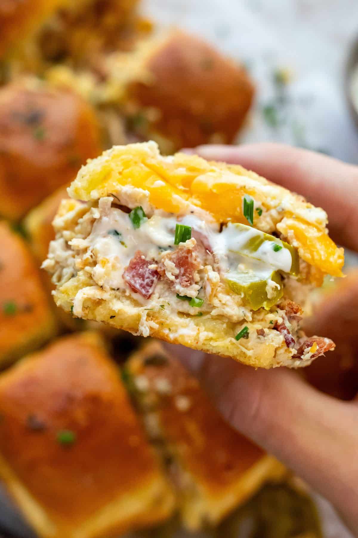 Slider buns stuffed with shredded chicken and bacon in a hand up close. 