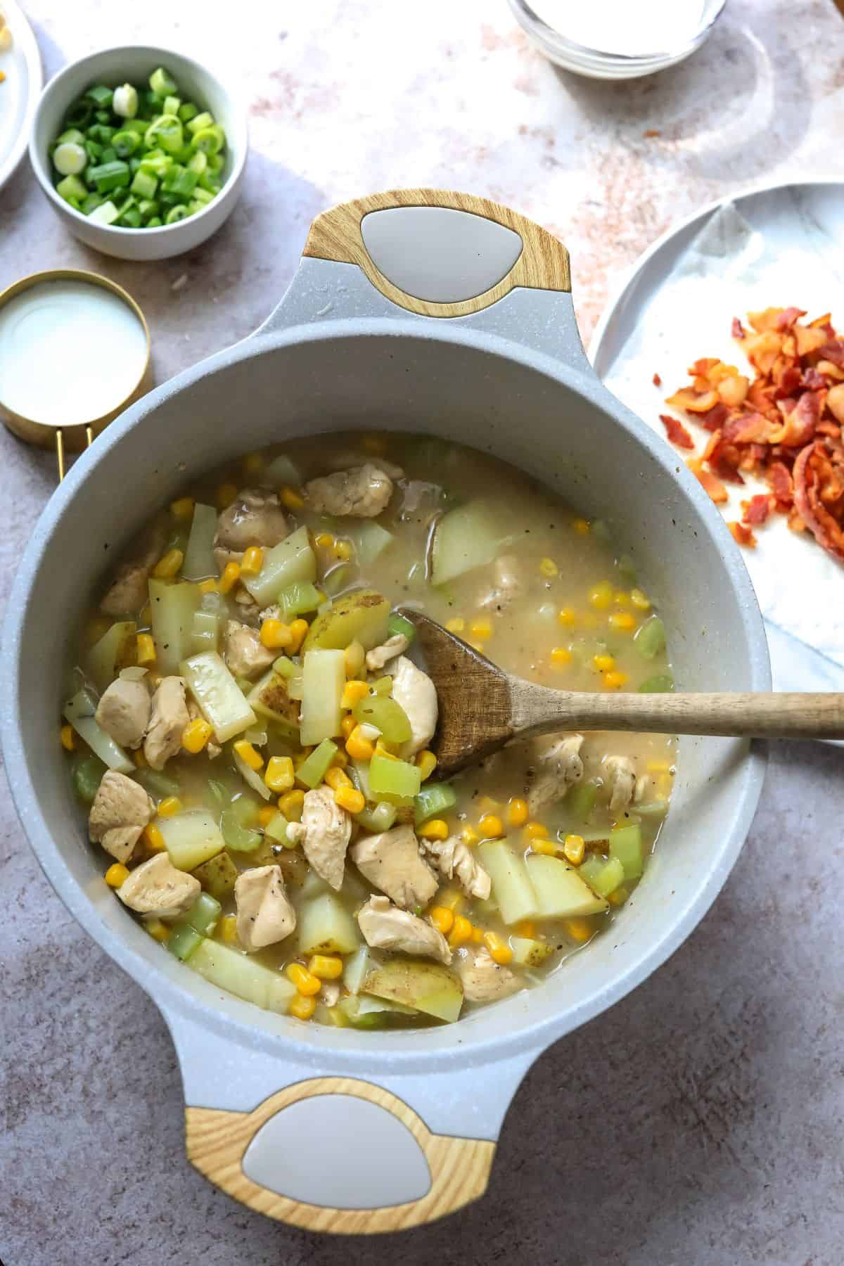 Grey soup pot with chicken corn chowder and a wooden spoon. 