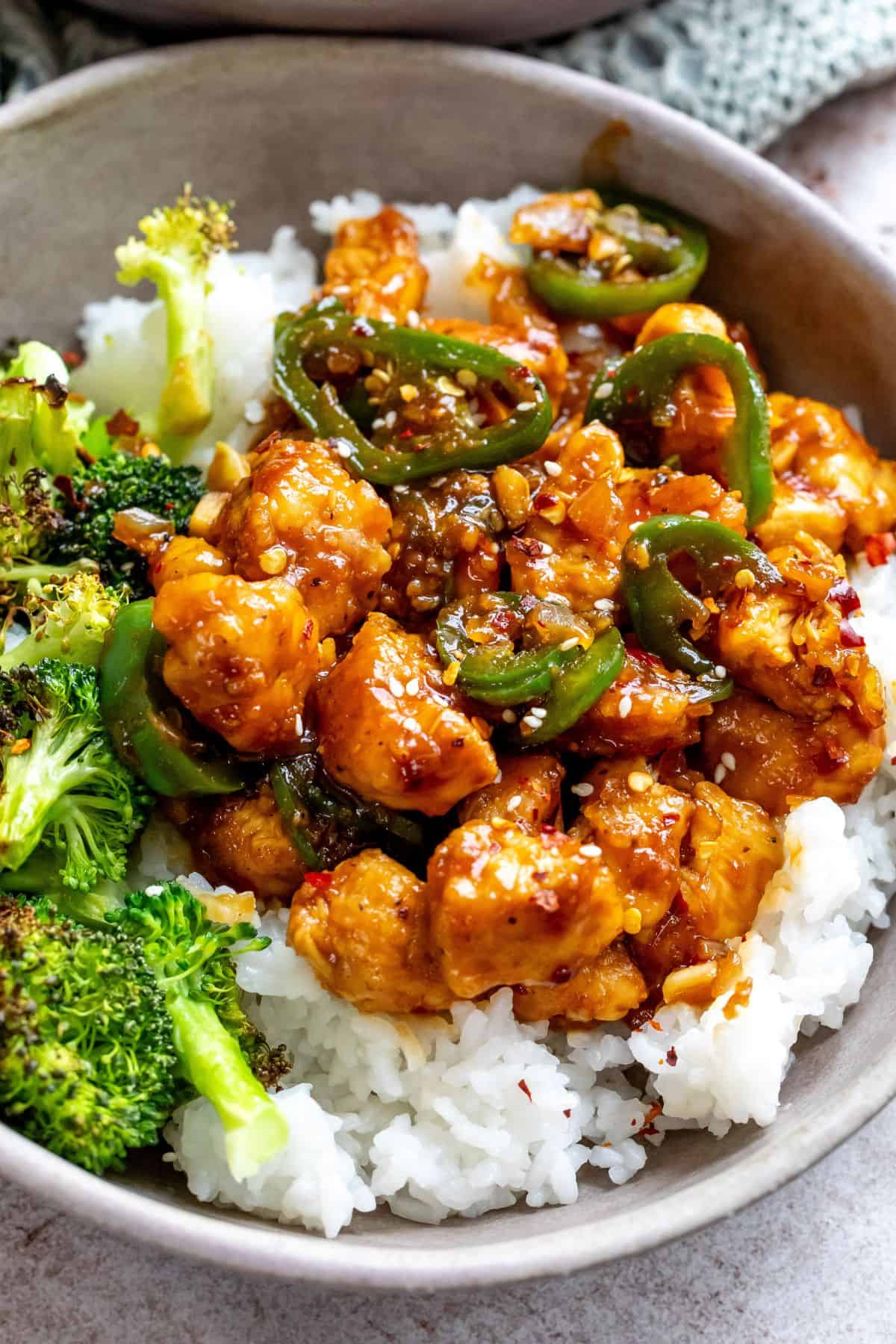 Grey ceramic bowl with jalapeño chicken recipe  and sauce served over rice with broccoli.