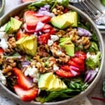 Ceramic bowl with green, strawberry, goat cheese all served as a salad. Balsamic dressing to the side.