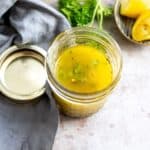 Glass jar with lemon honey dressing in it. Olive oil on the side.