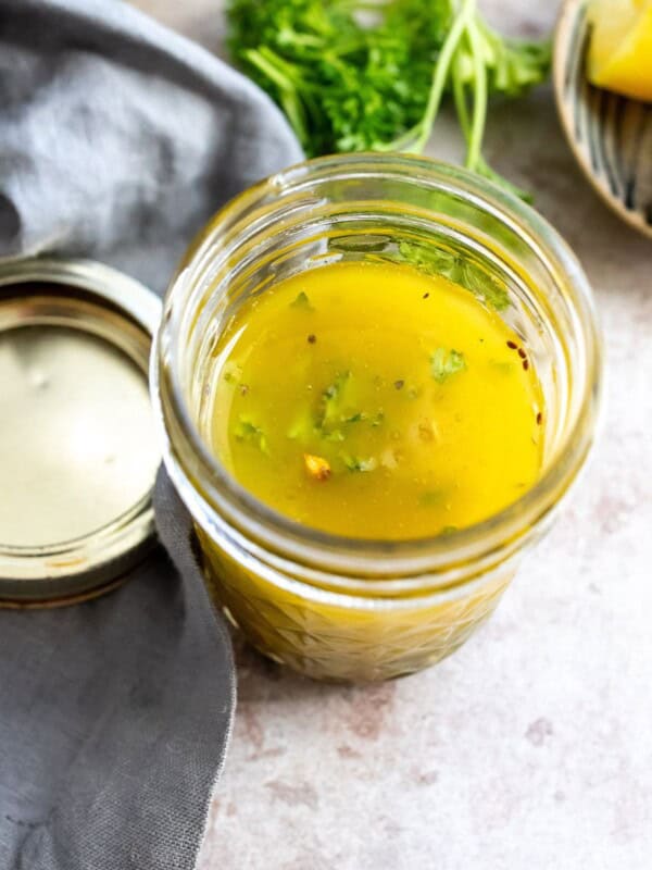 Glass jar with lemon honey dressing in it. Olive oil on the side.