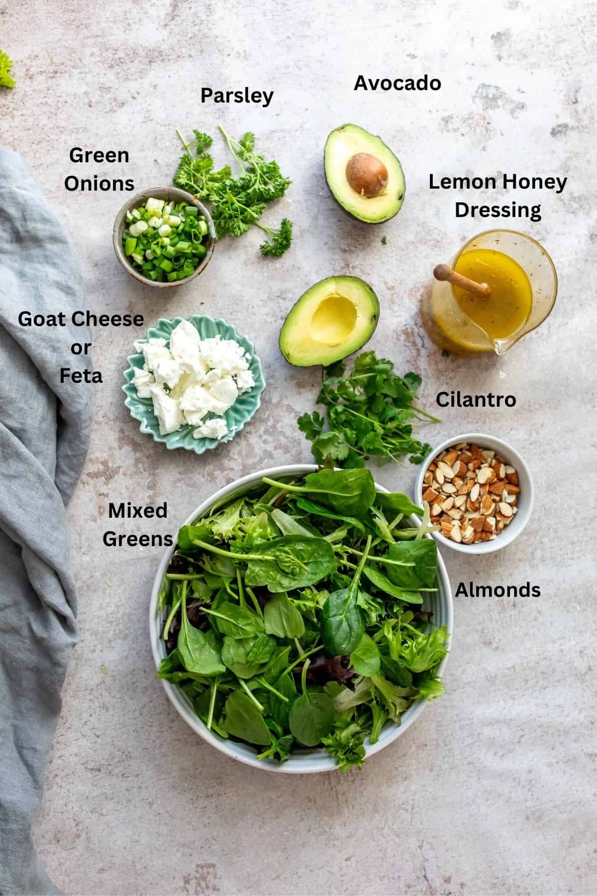 Ingredients needed to make mixed green salad in small bowls and on a counter. 