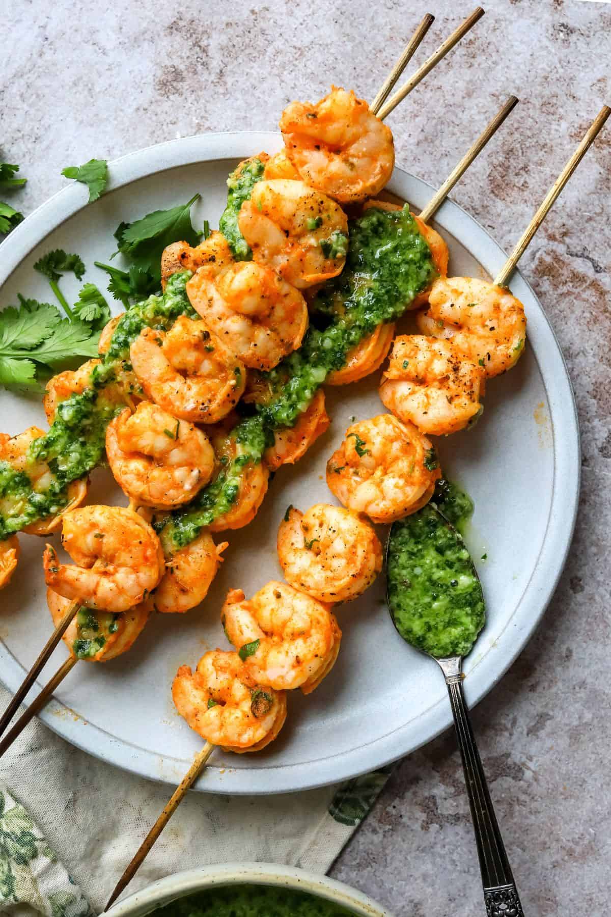 Shrimp Skewers in the Oven on a white plate with a fork and pesto. 