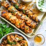 Baking sheet with spicy bang bang chicken skewers and a bowl on the side with air fried chicken skewers.