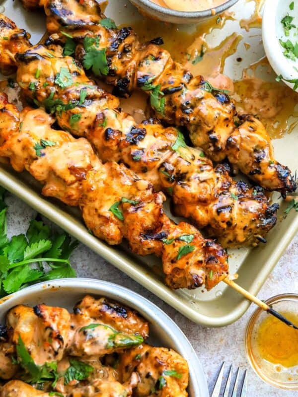 Baking sheet with spicy bang bang chicken skewers and a bowl on the side with air fried chicken skewers.