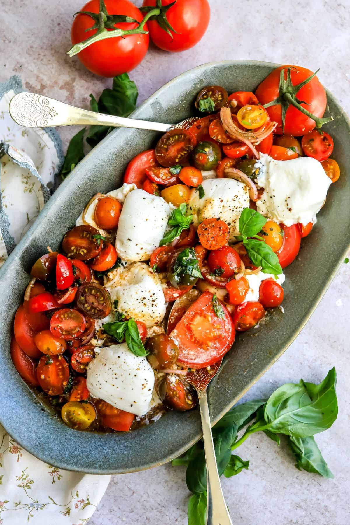 Green serving dish with tomatoes, burrata and basil. Lots of dressing and seasoning, 