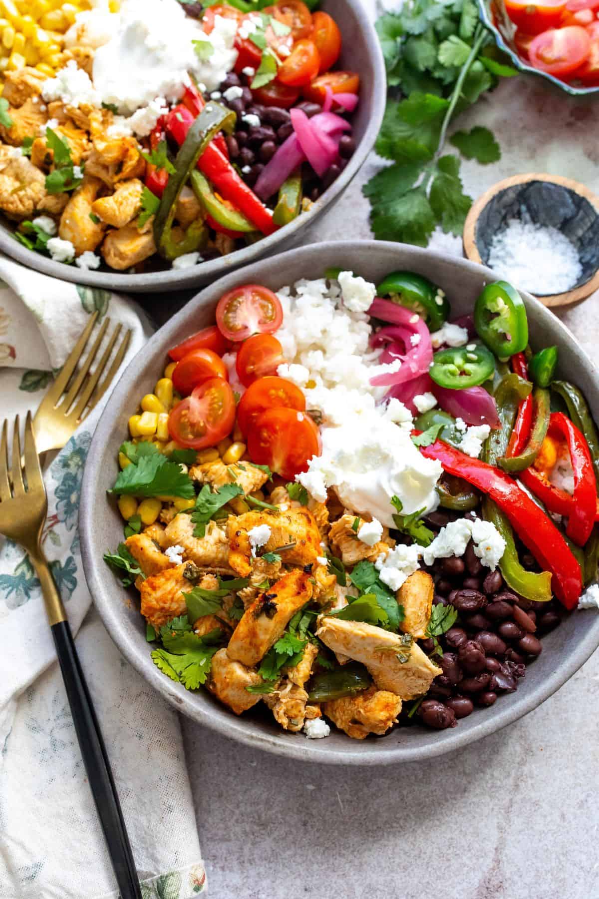 Grey ceramic bowls with cilantro lime chicken and lots of veggie toppings. Gold fork to the side. 