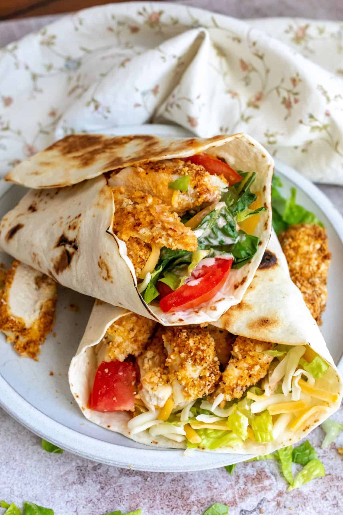 Crispy chicken in a wrap with lettuce and tomato on a plate. 