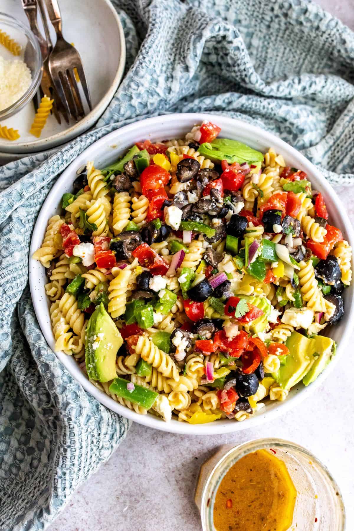 White ceramic bowl with zesty pasta salad in it with Italian dressing on the side. 