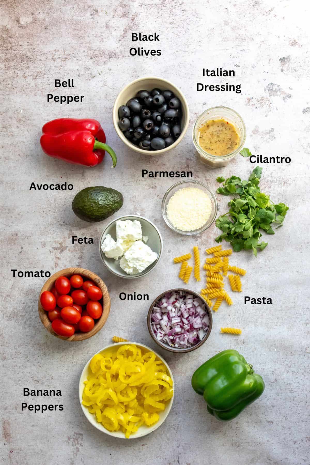 Ingredients on a counter in small bowls to make a zesty Italian pasta salad. 