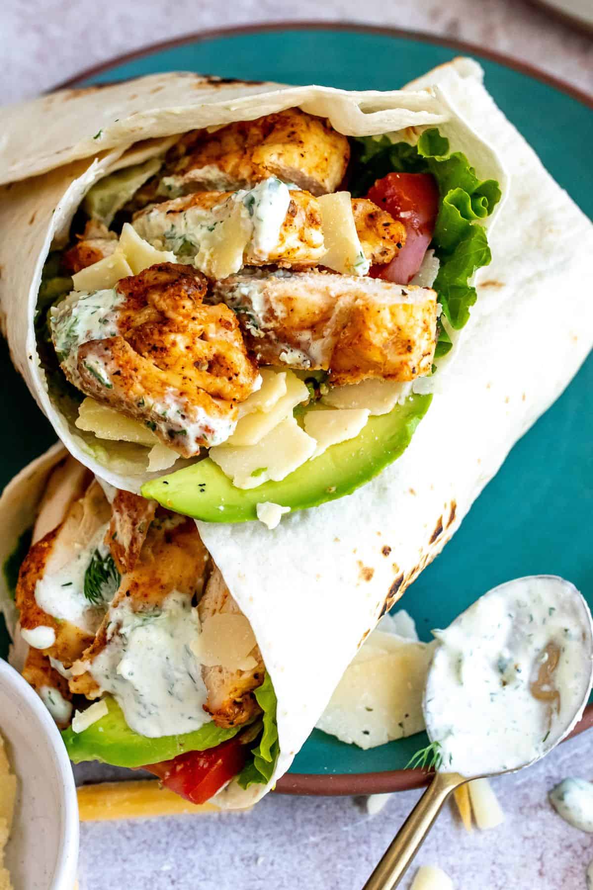 An image of two grilled chicken wraps on a plate with a spoon with ranch on the side.