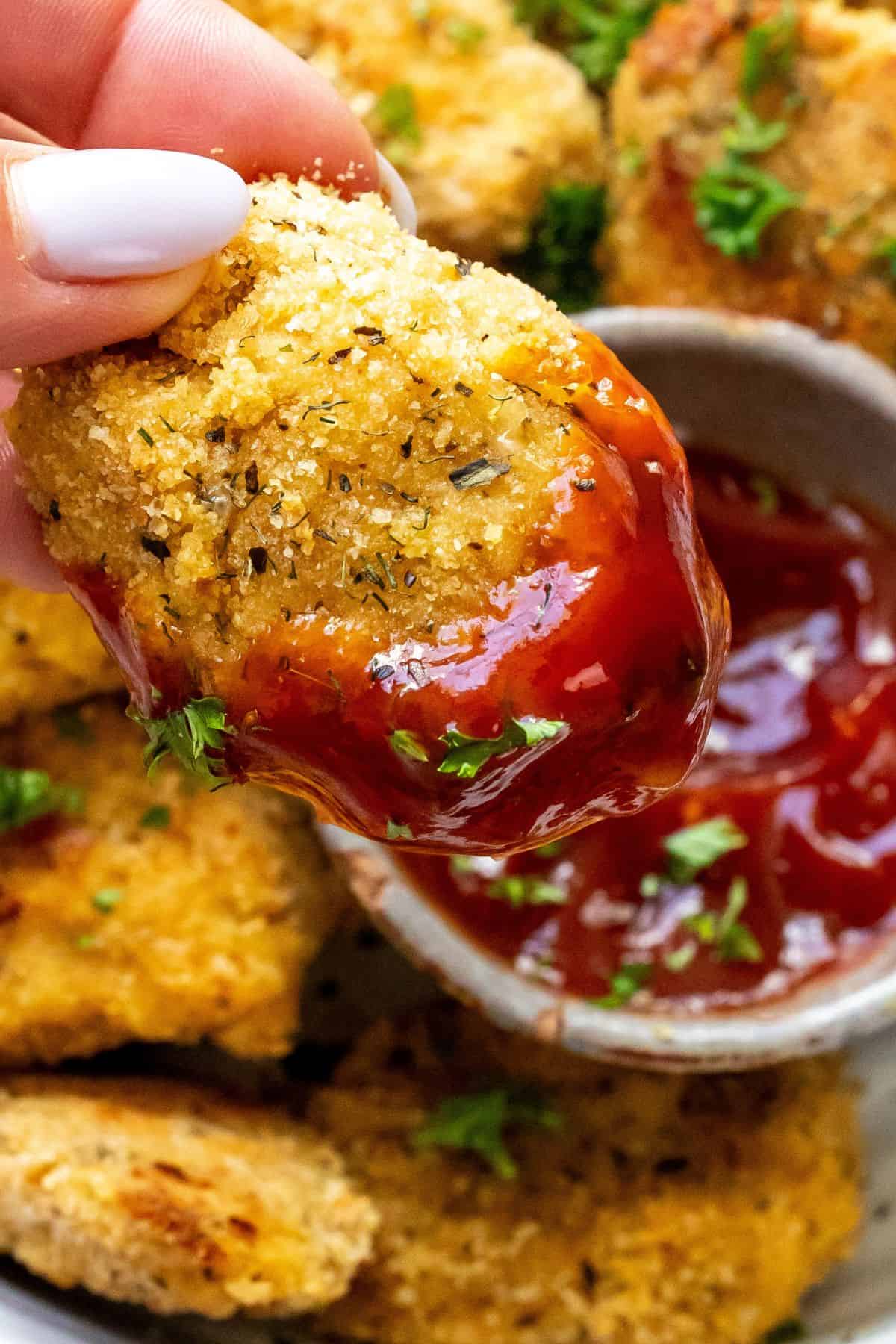 Close up of ground chicken nuggets dipped in ketchup. 