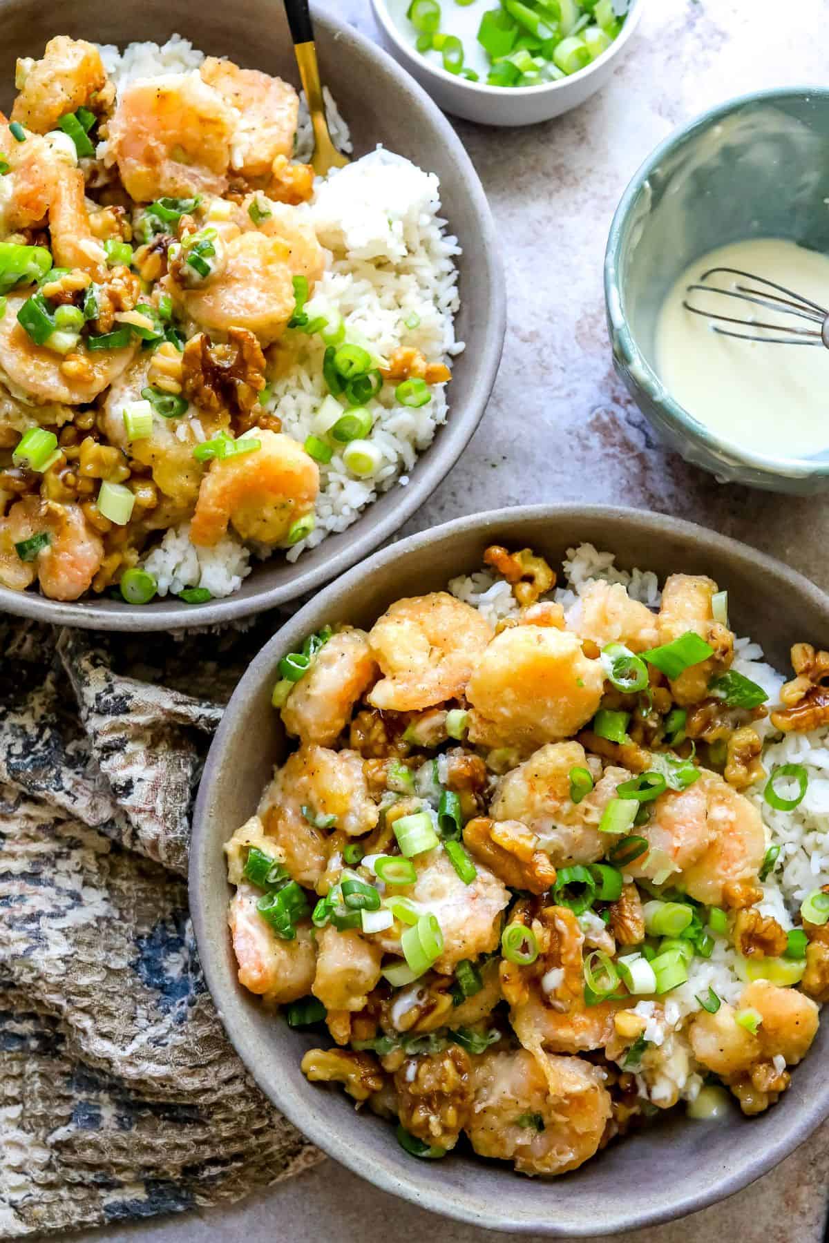 An image of two bowls of honey walnut shrimp with rice, garnished with green onions and candied walnuts.