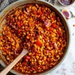 An overhead image of baked beans in a pot with a wooden spoon in the middle.
