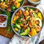 Grey bowl with mango, shrimp and salad in it. Cilantro and bacon to the side