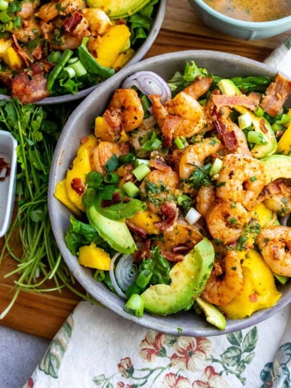 Grey bowl with mango, shrimp and salad in it. Cilantro and bacon to the side
