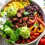 Ceramic bowl with steak and rice in it. Lots of toppings and a fork.