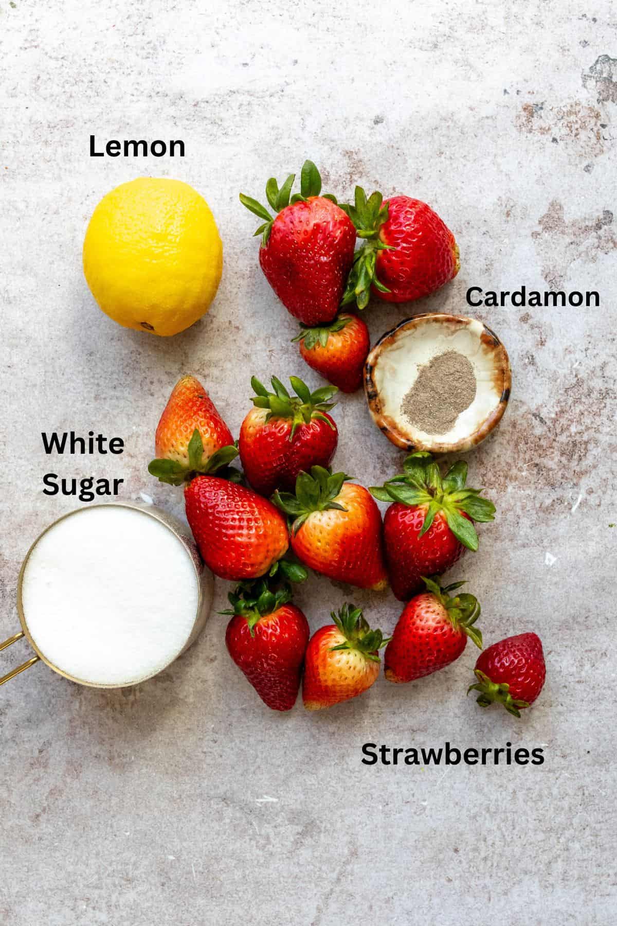 An overhead image of ingredients of strawberry jam recipe on a flat surface with labels on each ingredient.