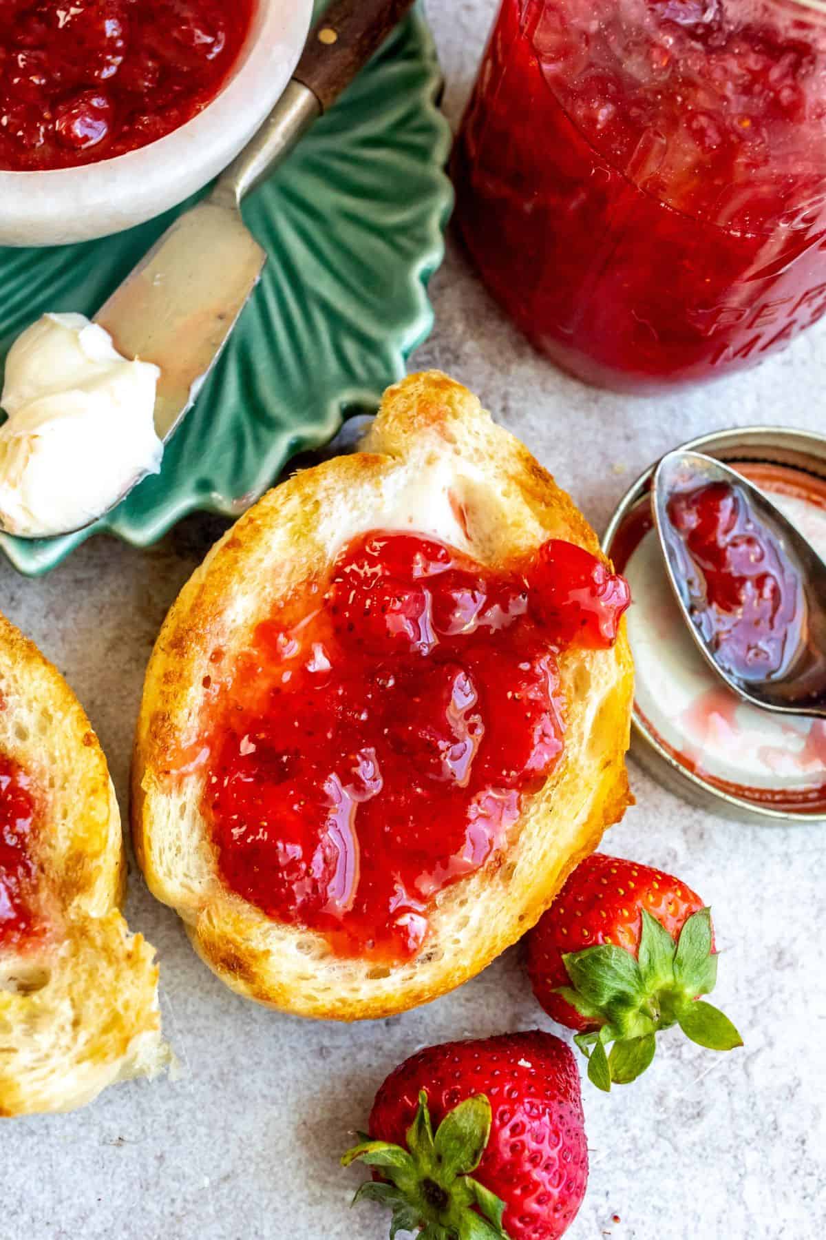 An overhead image of strawberry jam spread on toast, with a jar filled with jam on the side.