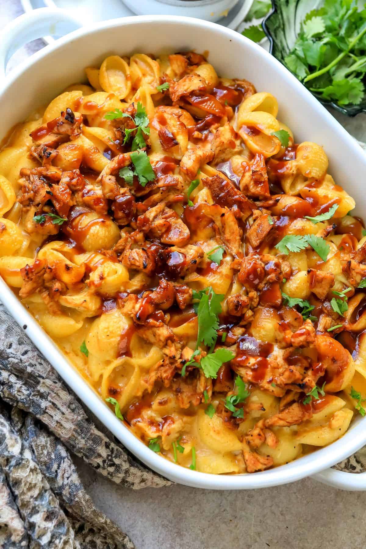 Noodles with cheese and bbq chicken baked into it in a white casserole dish. 
