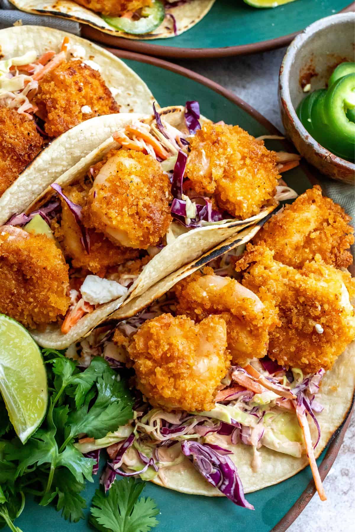 Up close photo of the baja shrimp tacos with a lime on the side on a green plate. 