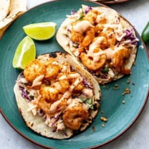 Green plate with baja shrimp tacos on them and limes to the side.
