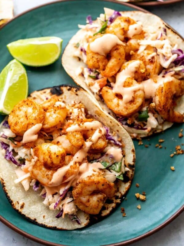 Green plate with baja shrimp tacos on them and limes to the side.