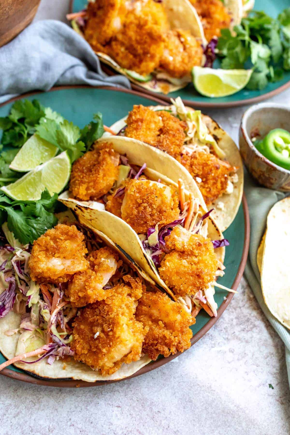 Baja shrimp tacos on a green plate with limes on the side. 