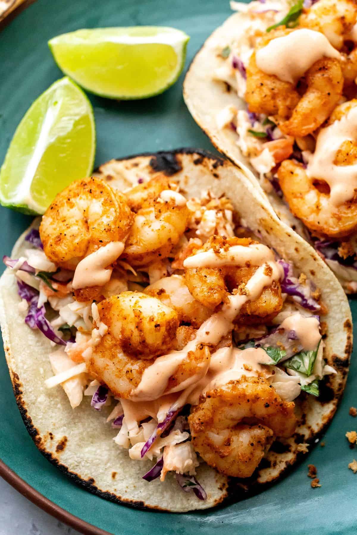 Up close photo of the baja shrimp tacos with a lime on the side on a green plate. 
